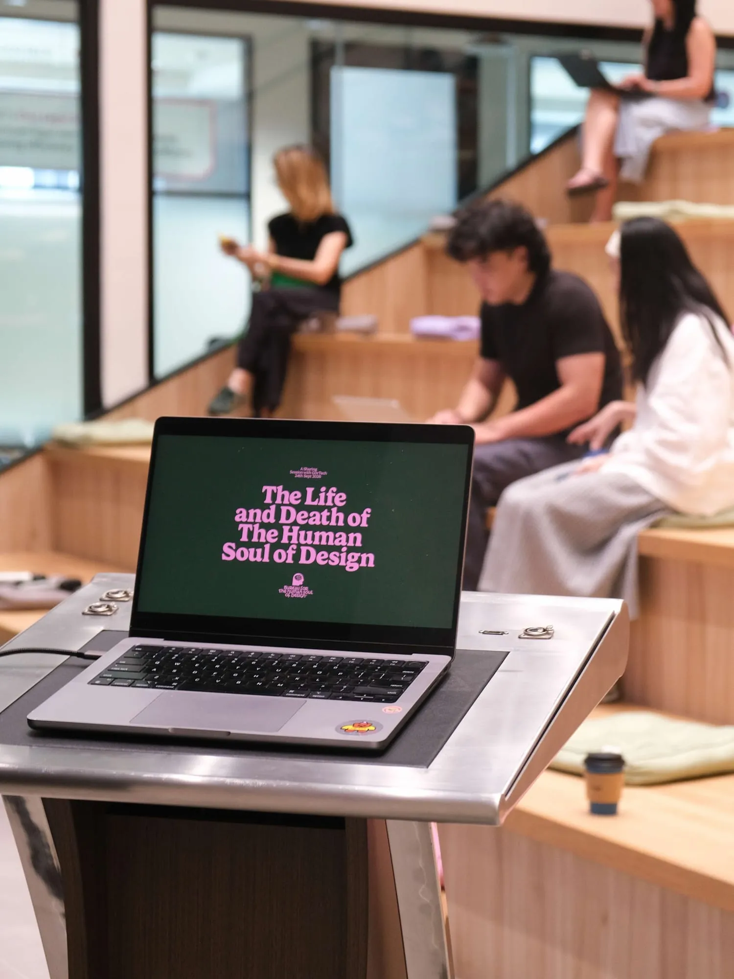Pann's laptop on the lectern showing the talk's title slide, with attendees seated behind.